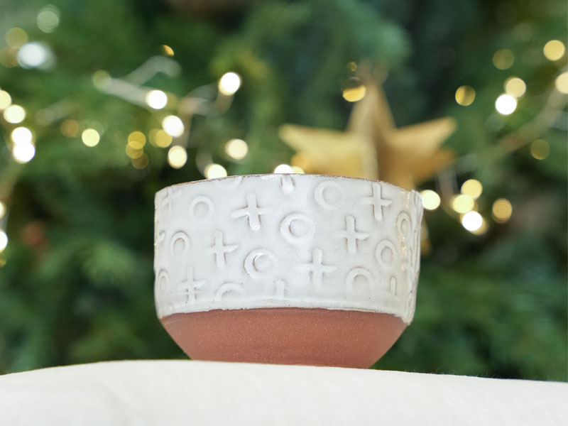 A ceramic bowl with white glazed sides decorated with Xs and Os in front of a Christmas tree