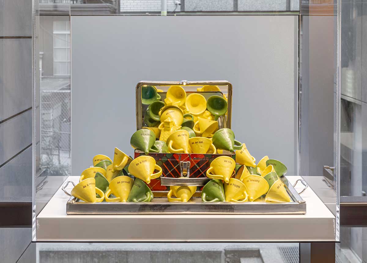 A glass vitrine with a ceramic sculpture in the form of a box filled with small yellow and green cones