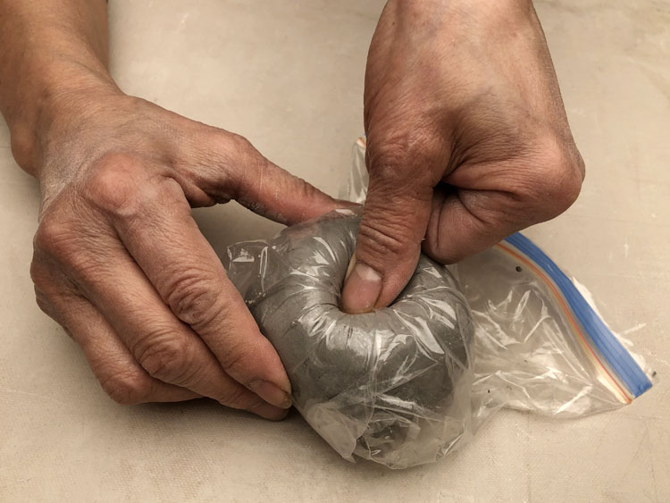 Hands pressing and squishing clay through a plastic bag