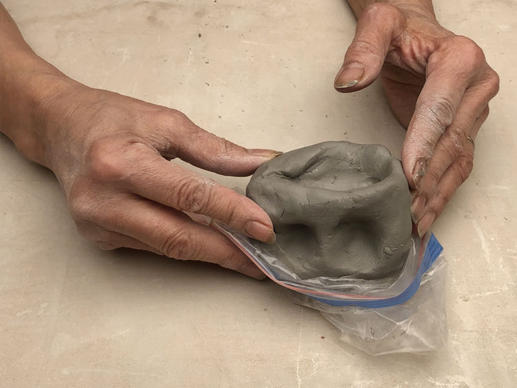 Hands removing clay sculpture from a plastic bag