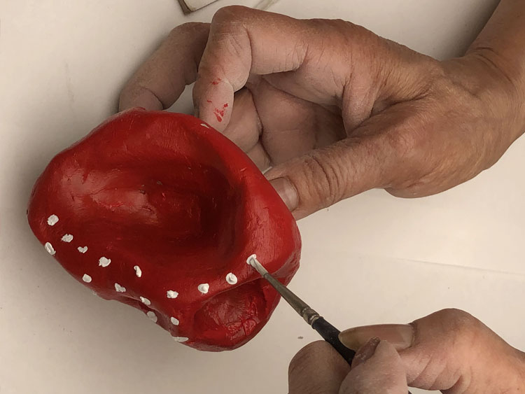 Painting white dots onto a red sculpture