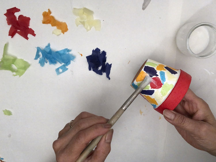 Gluing colourful pieces of tissue paper onto a pot in a mosaic pattern