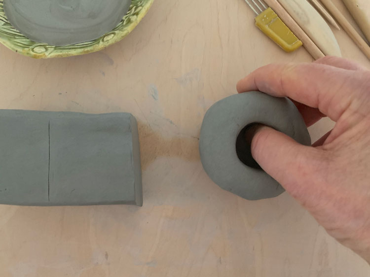 Hand pressing a hole into a ball of clay