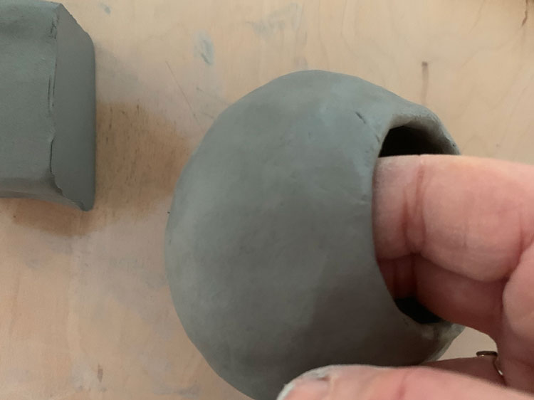 Hand pinching out the walls of a ball of clay