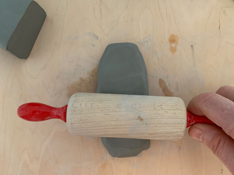 Rolling pin flattening a piece of clay