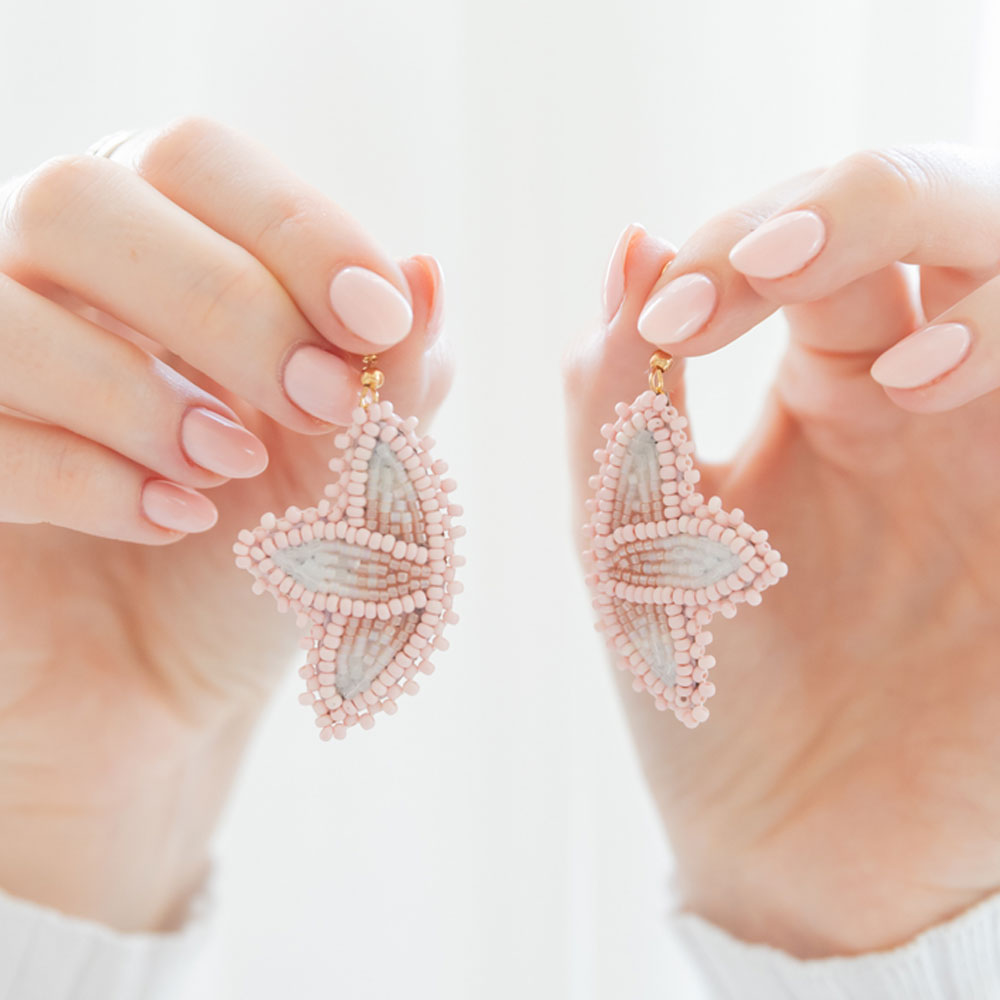 Hands holding a pair of pink beaded earrings in the form of flowers