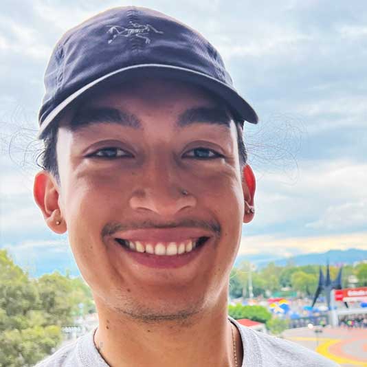A Latino man smiling at the camera wearing a baseball cap