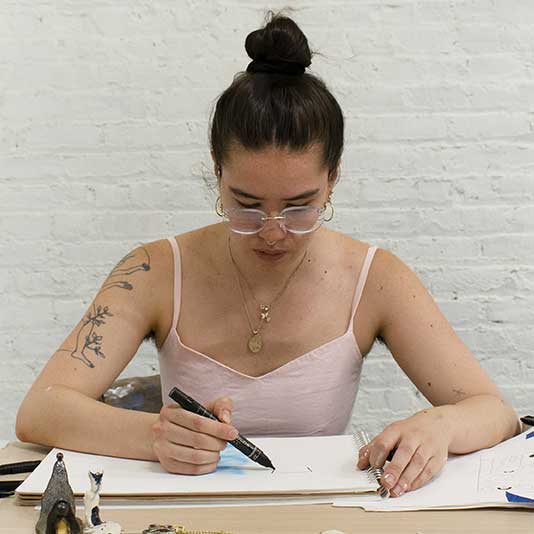 An Asian woman with a bun in her hair drawing at a desk