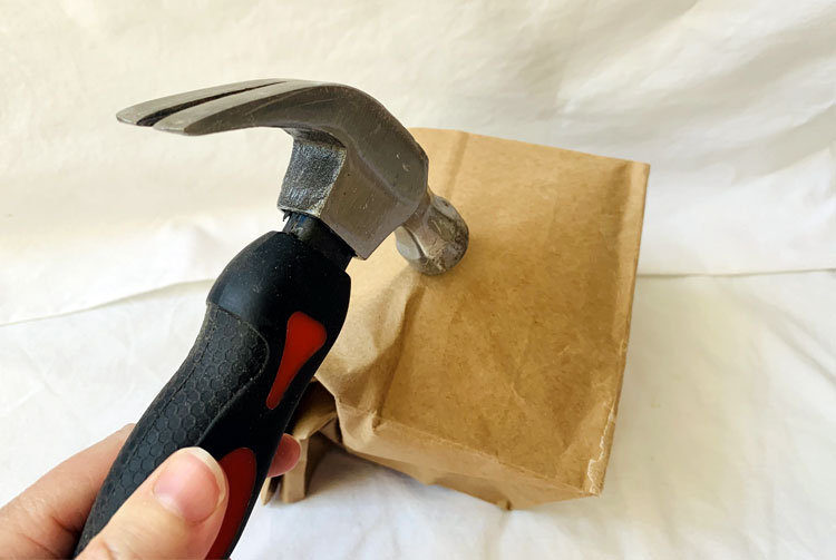 Hammer positioned over a paper bag with a clay pot inside
