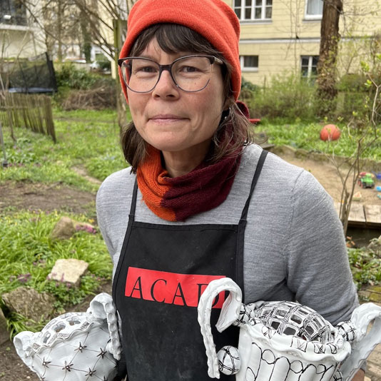 Artist Martina Lantin wearing an apron and a red toque holding two ceramic vessels