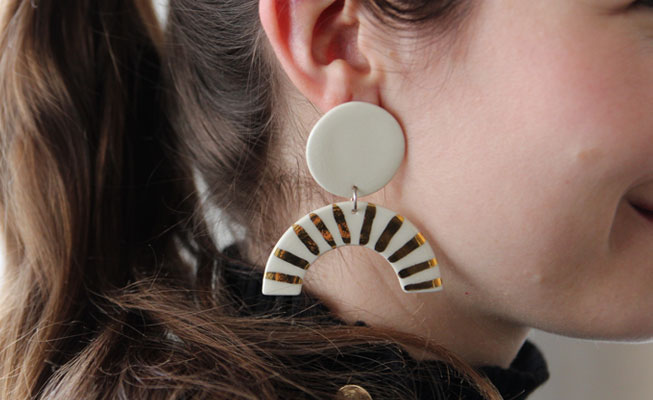 Woman wearing white ceramic earrings while a circular stud and dangling half moon with gold stripes
