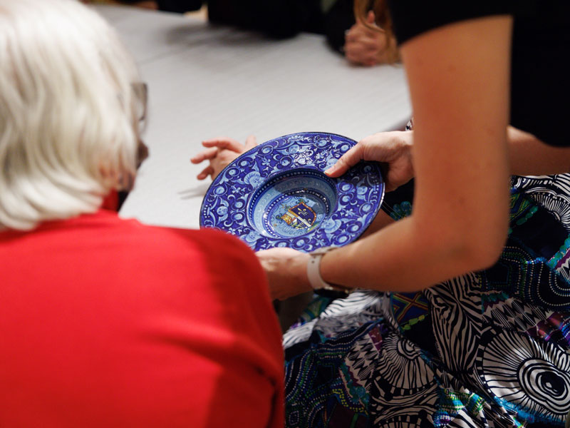 Hands holding a blue ceramic plate while another person looks at it