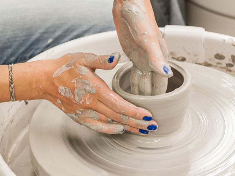 Hands of someone wearing blue nail polish using the pottery wheel