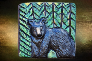 A low-relief carving of a black bear in a forest on a clay tile