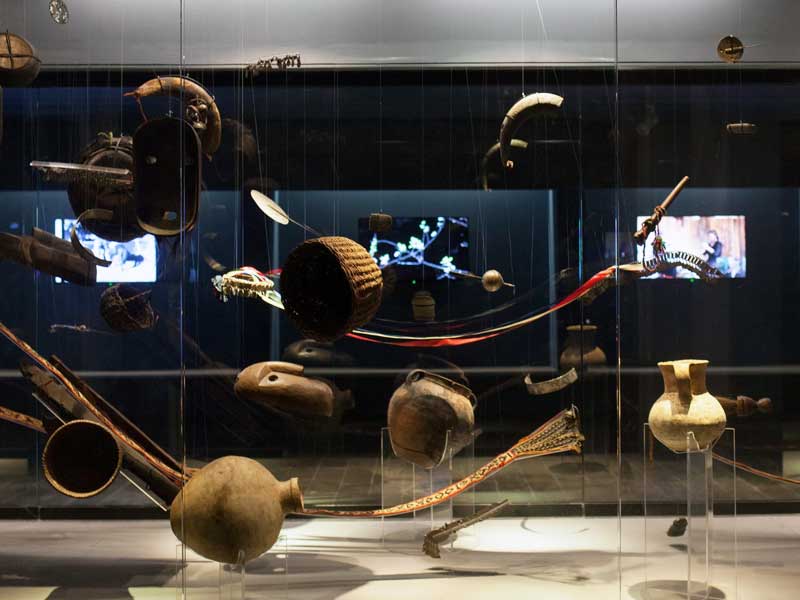 Indigenous belogings including pottery and textiles suspended in a glass case